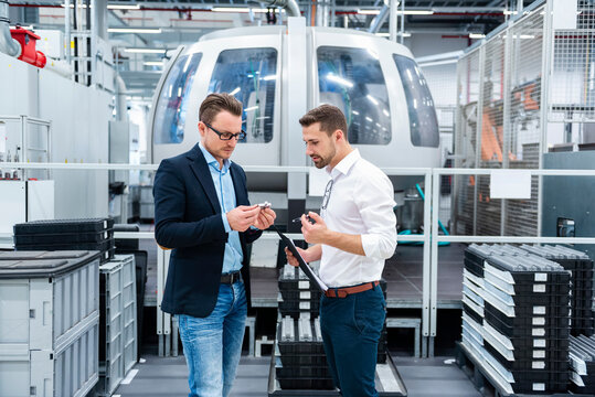 Two employees discussing notes in a production hall with machinery