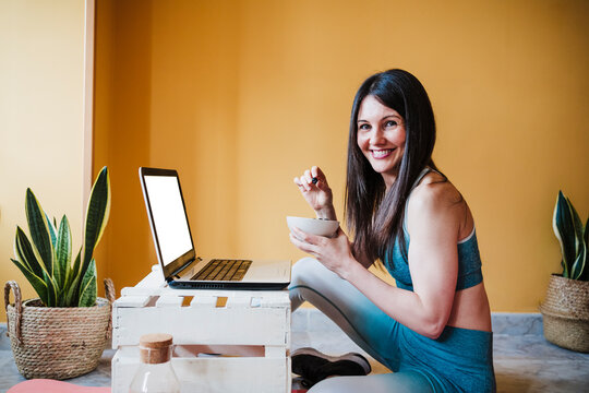 Cheerful woman holding bowl while sitting by laptop at home