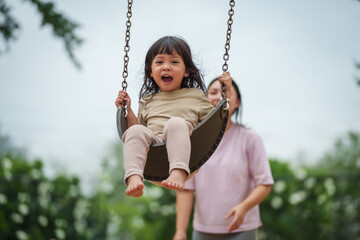 cheerful toddler girl with mother playing on a swing at playground