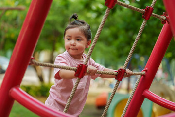 happy toddler girl playing with climbing ropes net at a outdoor playground in park