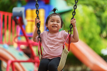 cheerful toddler girl playing on a swing at playground