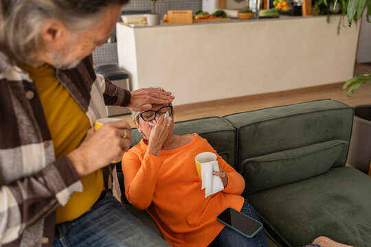 Senior couple at home with one person caring for the other who is sick on the sofa