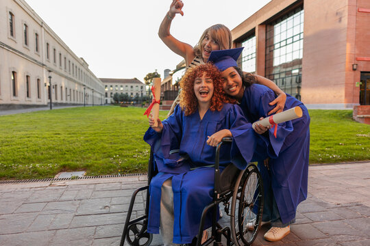 Graduation celebration on university campus with a mother and two graduates in cap and gown, one in a wheelchair