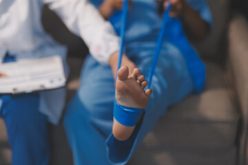 Confident physical therapist helps patient use resistance band stretching out his leg in clinic room.
