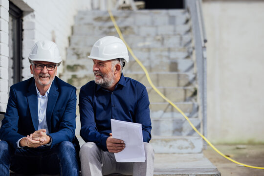Two engineers sitting on stairs at a construction site discussing plans