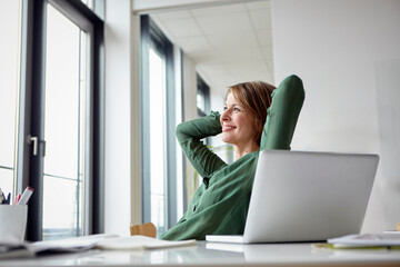 Businesswoman in green shirt relaxing at office desk with laptop