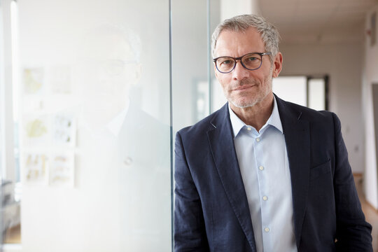 Businessman in an office wearing glasses and a suit smiling confidently