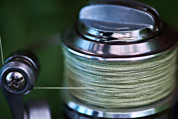 Close-up of a fishing reel with olive colored braided fishing line. Selective focus