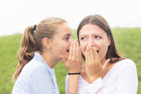 Blond woman gossiping in female friend's ear in nature