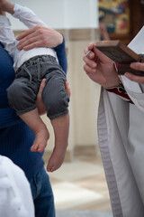 The close-up image shows an adult holding a baby in gray pants, while another person's hand...