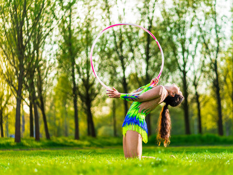 Young woman performing rhythmic gymnastics with a hoop in a green meadow outdoors