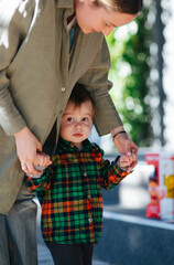 Mom and her son toddler in the park. Mom is holding kid hand, they are walking outdoor. Happy family dream concept. Mother and child together, lifestyle photo.