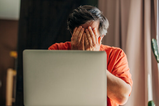 Man in orange shirt showing panic while looking at computer during financial
