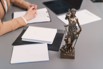 statue of themis on lawyer's desk. Woman lawyer, judge at work close-up, selective focus, blurred background. Advocate signs documents, paperwork