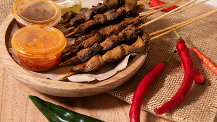 some skewers of satay and chili sauce on a wooden plate