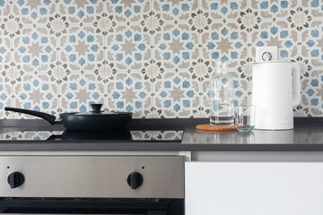 Contemporary kitchen interior. Ceramic induction cooktop with frying pan, white electric kettle, glass carafe with water