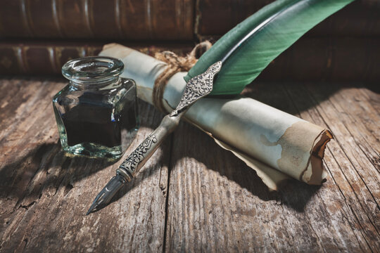 Quill pen, ink well and parchment paper scroll on desk with books