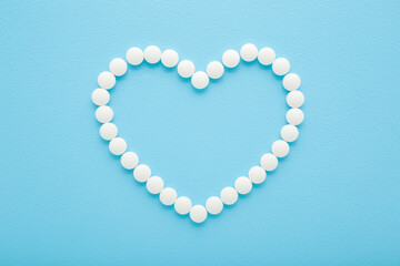Heart shape created from white pills on light blue table background. Pastel color. Closeup. Healthcare concept. Top down view.