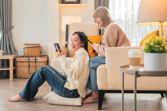 family concept Asian Elderly mother with white hair playfully combing her mature daughter's hair who sit on floor in a living room at home Beautiful moment of loving grown up daughter