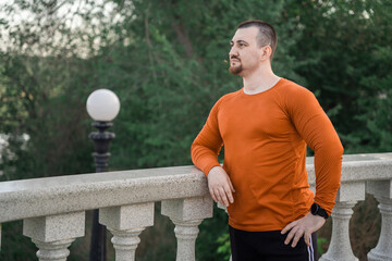 A man in workout clothes rests on a railing with a scenic view