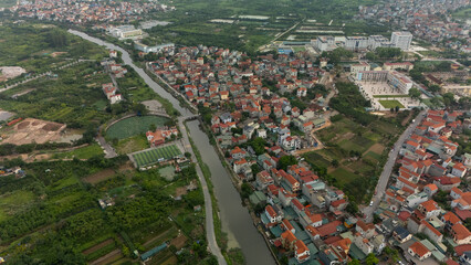 Top-down aerial view of a narrow canal winding through lush suburban housing, lined with tropical trees and adjacent garden plots