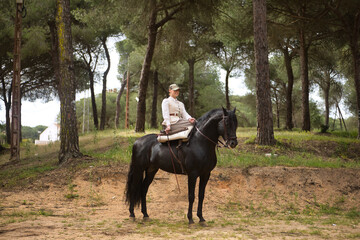 Young horsewoman riding her black Spanish thoroughbred horse, posing in the middle of the field....