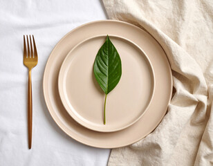 A solitary green leaf resting on a matte beige plate placed on a linen napkin.