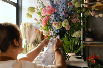 Middle-aged female florist in apron arranging fresh flowers for bouquet She ties a ribbon on the...