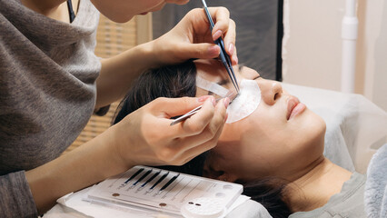 Young female southeast asian girl woman undergoes beauty procedure getting eyelashes extension at salon for eyes makeup health wellness, feeling satisfied
