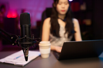 Woman recording podcast using professional microphone setup and laptop, with focus centered on the...