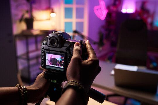 Photographer holding a professional camera, capturing scene decorated with vibrant lighting and modern setup. Blurred background enhances focus on camera