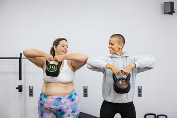 Personal trainer supporting overweight woman lifting kettlebell in gym