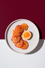 Rodajas de naranja sanguina sobre un plato blanco con fondo blanco y granate. Vista superior