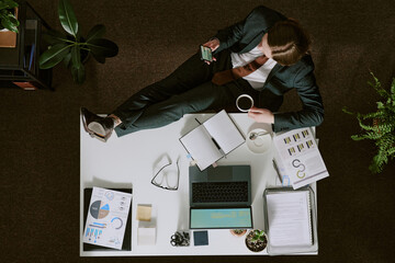 Obraz premium Businessperson reviewing documents while sitting at desk, surrounded by office supplies and charts, creating productive workspace environment