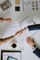 Plakat Business people shaking hands over meeting table with documents, graphs, and a cup of coffee. Image depicting agreement, cooperation, and successful negotiation in professional setting