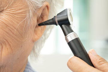 Audiologist or ENT doctor use otoscope checking ear of asian senior woman patient treating hearing...