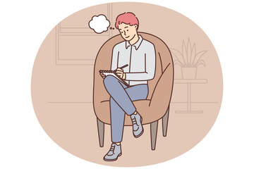 Adult man sits in cozy chair and makes notes in notebook making plans for day