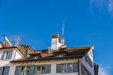 European Rooftop: Smoking Chimney with Animal Silhouette Against Clear Blue Sky.Clear Blue Sky Over Historic Building with Smoking Chimney and Unique Roof Decor.