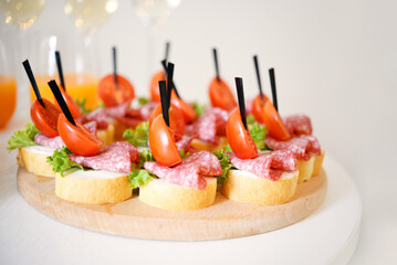 canapes with cherry tomatoes, salami, herbs and bread are on a wooden plate. close up	