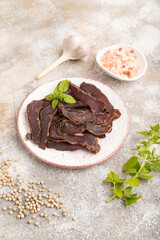 Armenian Basturma dried meat on plate with pepper and herbs on brown concrete. Side view