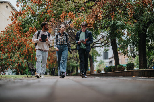 A group of students walking and discussing their studies outdoors on a scenic campus path surrounded by autumn trees, promoting collaboration and education in a natural setting. - Powered by Adobe