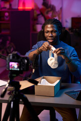 African American man sitting at desk, reviewing new headphones model on livestream with keen concentration, camera equipment, in a well-lit indoor setting