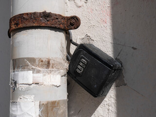 Key safe (outdoor key lock box) in a tourist apartment, attached to a pipe with a rusty hook, waiting to be opened next to a white wall