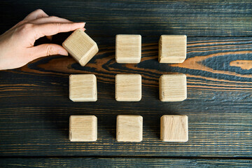 Hand choosing blank wooden cube from neatly arranged blocks