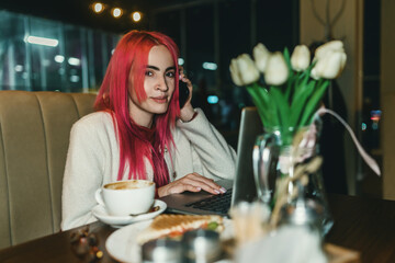 A woman with red hair is sitting with a laptop in a cafe