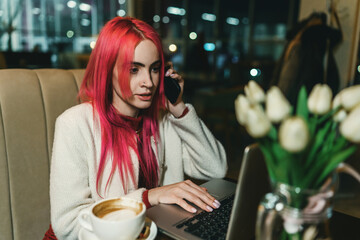 A woman with red hair is sitting with a laptop in a cafe