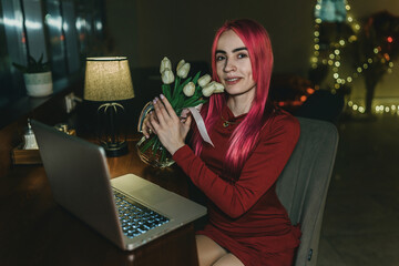 A girl with red hair and a red dress is sitting at a laptop in a cafe