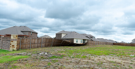 Panorama view privacy brick and stone corner with collapsed wooden fence by strong winds damages at residential area suburban houses in Princeton, Texas, stormy cloudy, tornado insurance claims