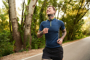 Handsome young man enjoys a refreshing jog along a tree lined path in the morning sunlight
