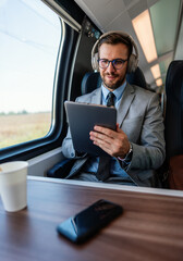 Young businessman wearing headphones and using digital tablet while traveling by train, enjoying music and staying productive during his commute